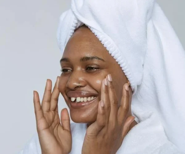 black woman in a robe touching her face that's glowing from acne skincare products