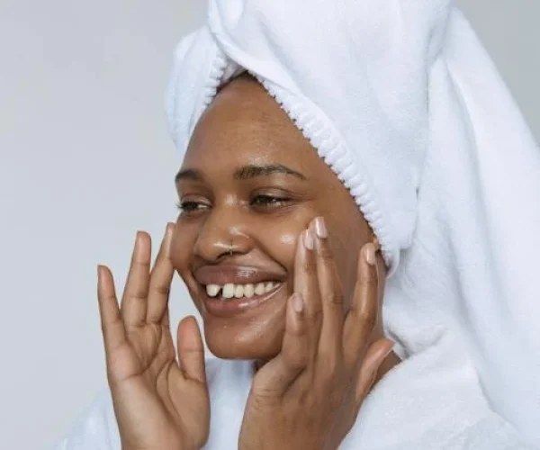 black woman in a robe touching her face that's glowing from acne skincare products WHat is hyaluronic acid